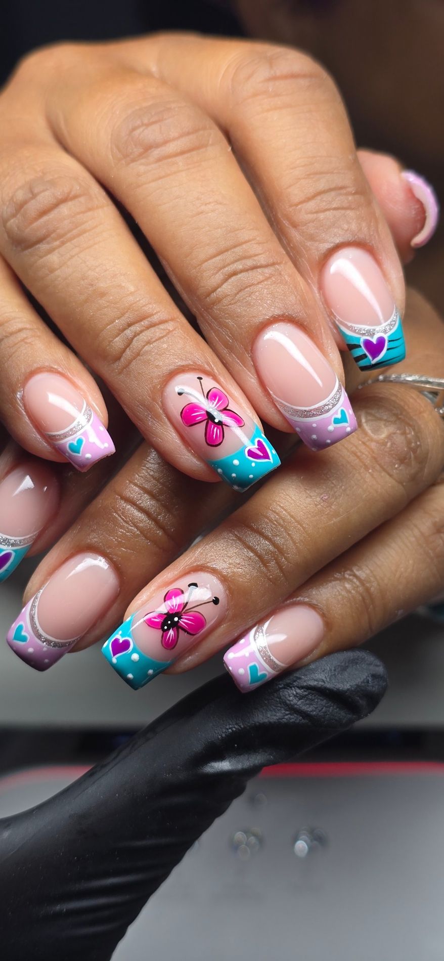 Uñas francesas con mariposa fucsia y puntas turquesa y lila