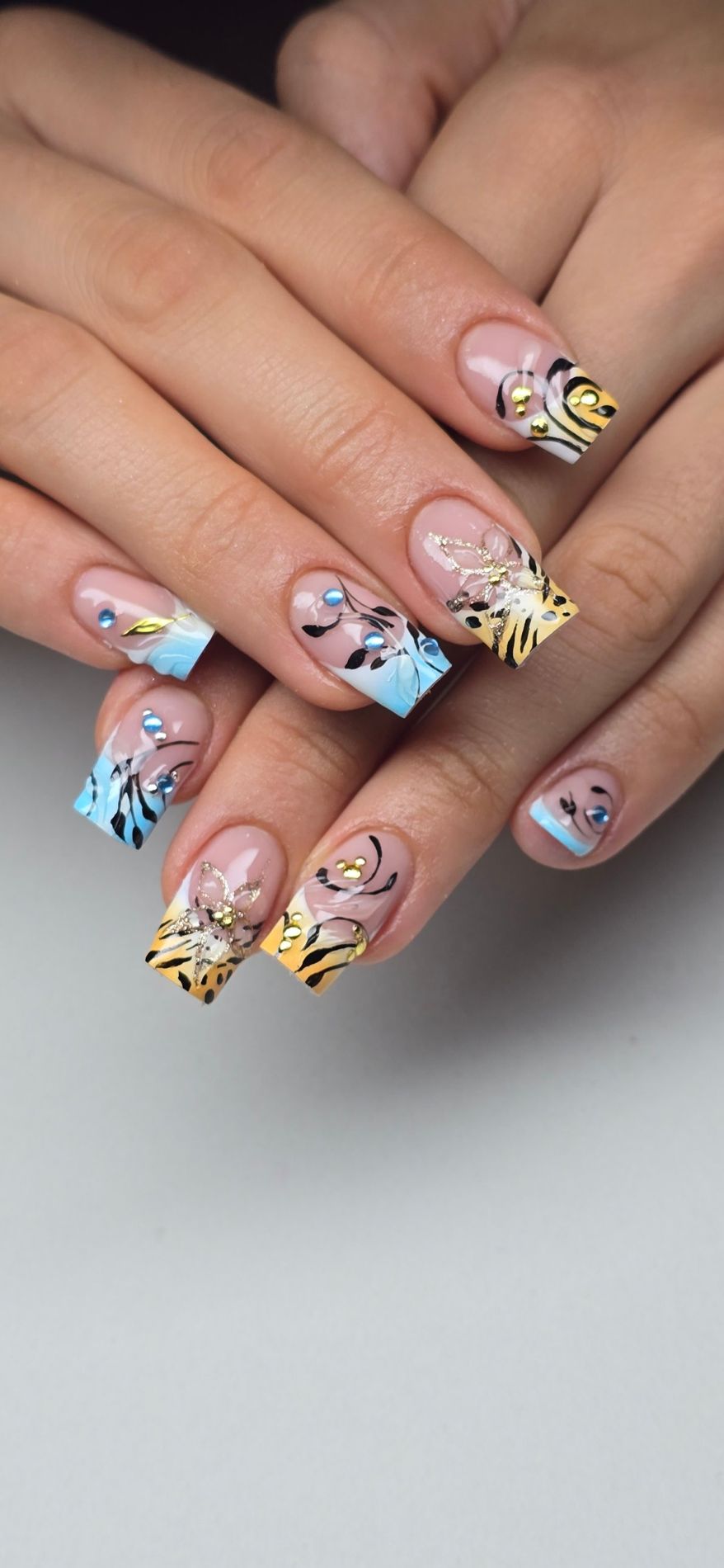 Uñas francesas con degradado azul y naranja, flores y estampado de tigre